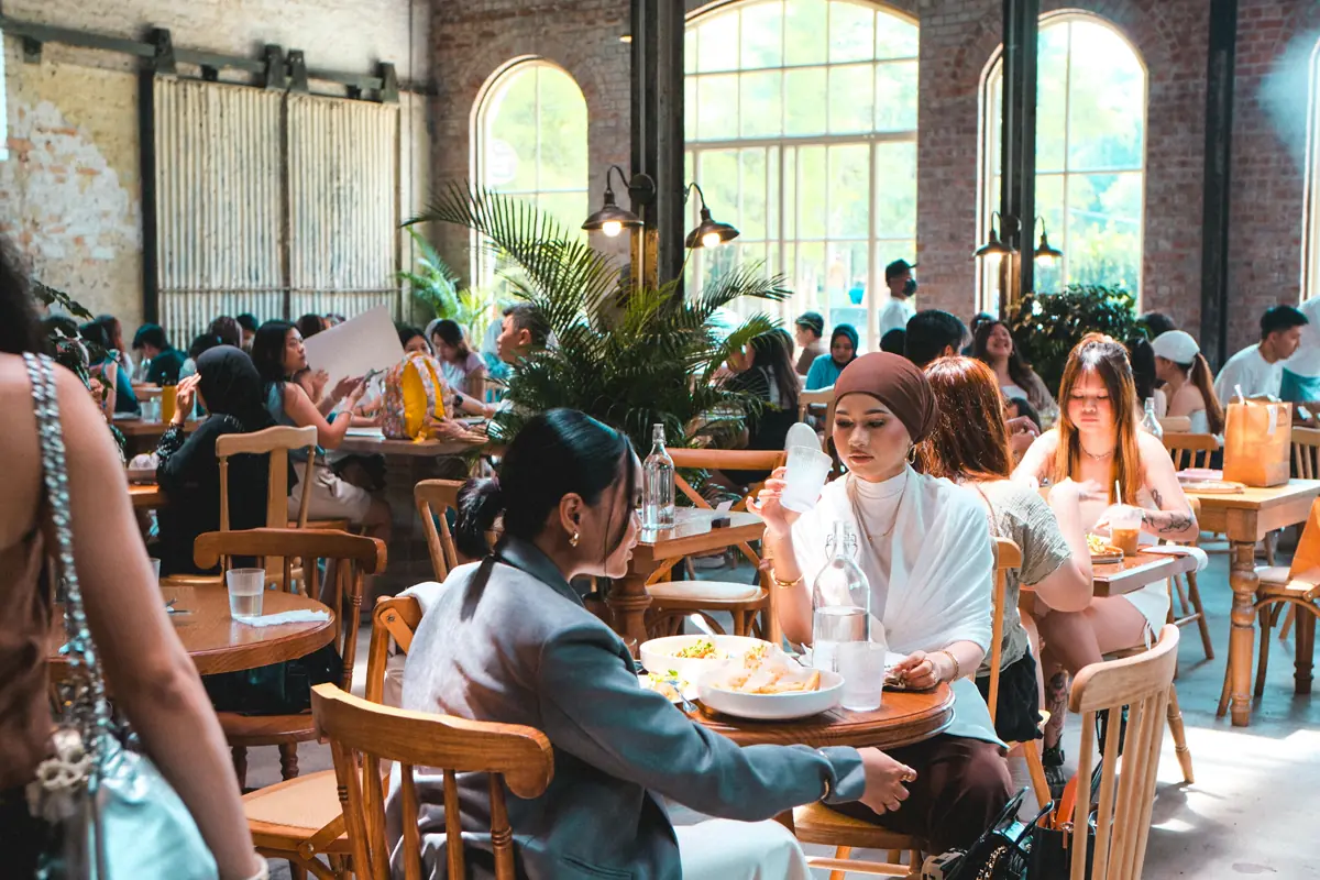Gäste essen und unterhalten sich an Tischen in einem vollen, sonnigen Restaurant